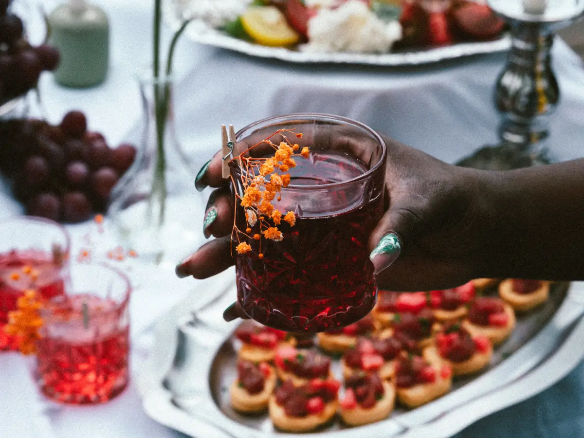 Brunch élégant avec verre rouge et fleur jaune Main tenant un verre rouge avec une fleur jaune à l’intérieur, brunch flou en arrière-plan avec un titre et un texte.
